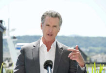 FBI Knocks: Newsom’s Inner Circle Scrutinized Man speaking with microphone outdoors.