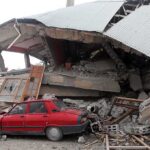 Quake Death Toll Bombshell — Scientists Sound 100,000 Alarm A red car parked next to a collapsed building with debris scattered around