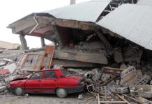 A red car parked next to a collapsed building with debris scattered around
