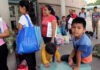Grieving Moms vs Congress Showdown People waiting outside carrying bags, boys sitting and playing.