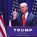 Media Spin Erupts After Lindsey Graham’s Death Man speaking at podium with USA flags behind him.