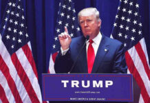Media Spin Erupts After Lindsey Graham’s Death Man speaking at podium with USA flags behind him.