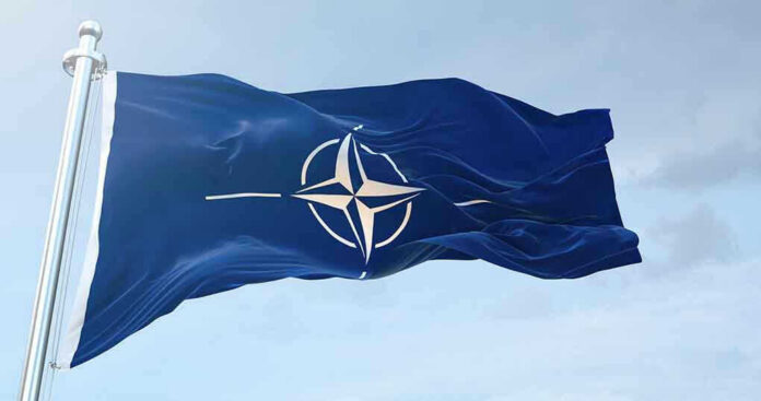 1633919905 NATO flag waving against blue sky.