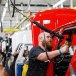 Worker assembles red vehicle on factory line