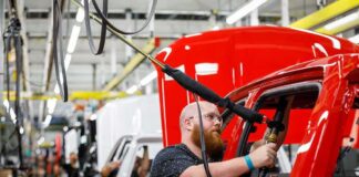 Worker assembles red vehicle on factory line