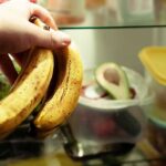 Banana Crates, Billion-Dollar Blow Hand holding two ripe bananas in a refrigerator