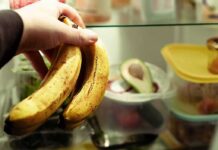 Hand holding two ripe bananas in a refrigerator