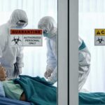 Outbreak Escalates, First Vaccine Given Healthcare workers in hazmat suits treat a patient in a quarantine room