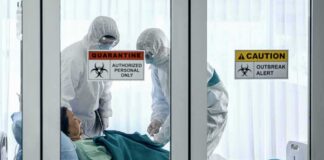 Healthcare workers in hazmat suits treat a patient in a quarantine room