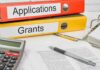 Two binders labeled Applications and Grants on a desk with a calculator and papers