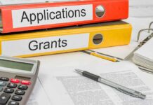 UC Riverside Picks Winners — US Citizens Last? Two binders labeled Applications and Grants on a desk with a calculator and papers