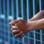 Close-up of clasped hands resting on a blue fence
