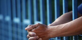 Close-up of clasped hands resting on a blue fence