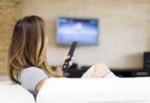 Prison To Prime Time—Seriously? A woman sitting on a sofa, holding a remote control and watching television
