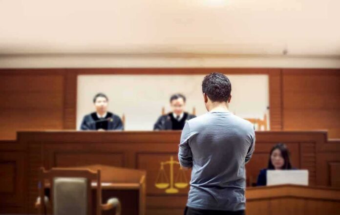 shutterstock_1049504825 defendant stands before judges in a courtroom