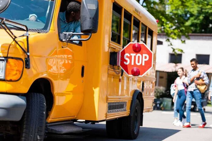 shutterstock_1160987455 School bus with extended stop sign near students on sidewalk