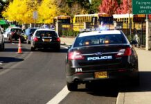 School Threat Suspect Walks — Days Before Class Starts Police cars with lights on near school buses on a city street