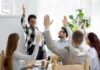 Team in meeting raising hands around a smiling presenter