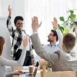 Team in meeting raising hands around a smiling presenter