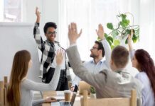 Race-Based Pay Bombshell Hits School Board Team in meeting raising hands around a smiling presenter