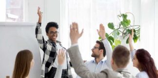 Team in meeting raising hands around a smiling presenter