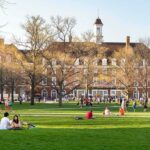 Foreign Cash Shadows Top Campuses Students relaxing on a campus quad in front of a brick academic building