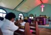 Congregants clapping inside a church with a glowing cross