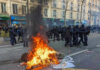 Milan Erupts, Meloni Doubles Down Fire burning on the street amid police presence.