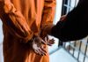 Brazil Erupts: Top Judge Targets Bolsonaro Clan Prisoner in orange jumpsuit handcuffed by officer