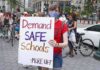 Person wearing mask holds protest sign reading Demand SAFE Schools