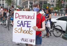 Person wearing mask holds protest sign reading Demand SAFE Schools