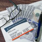 Surprise Medicare Payout Hits Next Week Medicare card on paperwork with cash, glasses, and a pen
