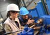 Two workers operating a metal lathe in a workshop