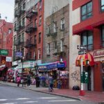 Pete Davidson Torches ‘Fake Staten Island’ City street with brick buildings, fire escapes, and busy storefronts